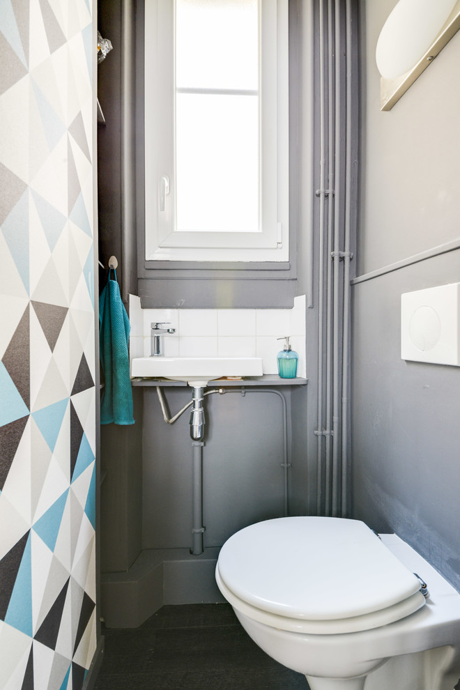 Small contemporary powder room in Paris with a wall-mount toilet, white tile, grey walls, a wall-mount sink, grey floor, grey cabinets, ceramic tile, vinyl floors and white benchtops.