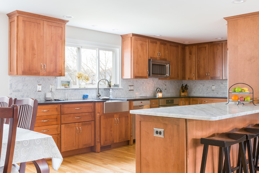 Inspiration for a mid-sized transitional u-shaped medium tone wood floor eat-in kitchen remodel in Boston with a farmhouse sink, beaded inset cabinets, medium tone wood cabinets, marble countertops, gray backsplash, marble backsplash, stainless steel appliances, a peninsula and gray countertops