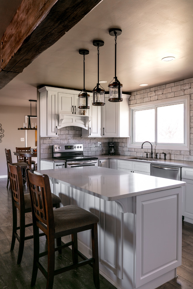 Inspiration for a mid-sized rustic u-shaped laminate floor and brown floor open concept kitchen remodel with an undermount sink, raised-panel cabinets, white cabinets, quartzite countertops, white backsplash, brick backsplash, stainless steel appliances, an island and gray countertops
