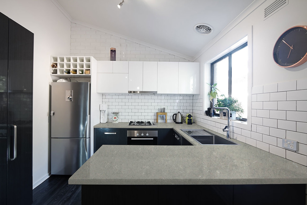 Design ideas for a mid-sized transitional u-shaped open plan kitchen with a double-bowl sink, flat-panel cabinets, white cabinets, quartz benchtops, white splashback, subway tile splashback, stainless steel appliances, dark hardwood floors, a peninsula and black floor.