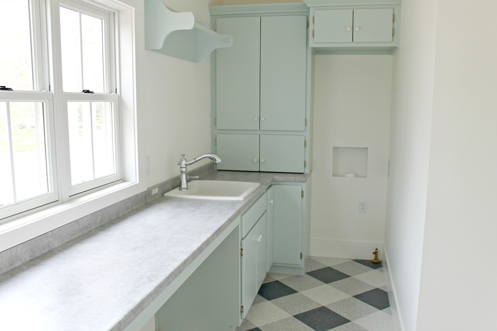 Mid-sized country l-shaped dedicated laundry room in Other with a drop-in sink, flat-panel cabinets, green cabinets, laminate benchtops, white walls, ceramic floors, a stacked washer and dryer and multi-coloured floor.