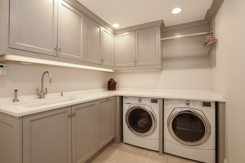 Design ideas for a mid-sized transitional l-shaped dedicated laundry room in Chicago with an undermount sink, recessed-panel cabinets, grey cabinets, solid surface benchtops, grey walls, ceramic floors, a side-by-side washer and dryer and beige floor.