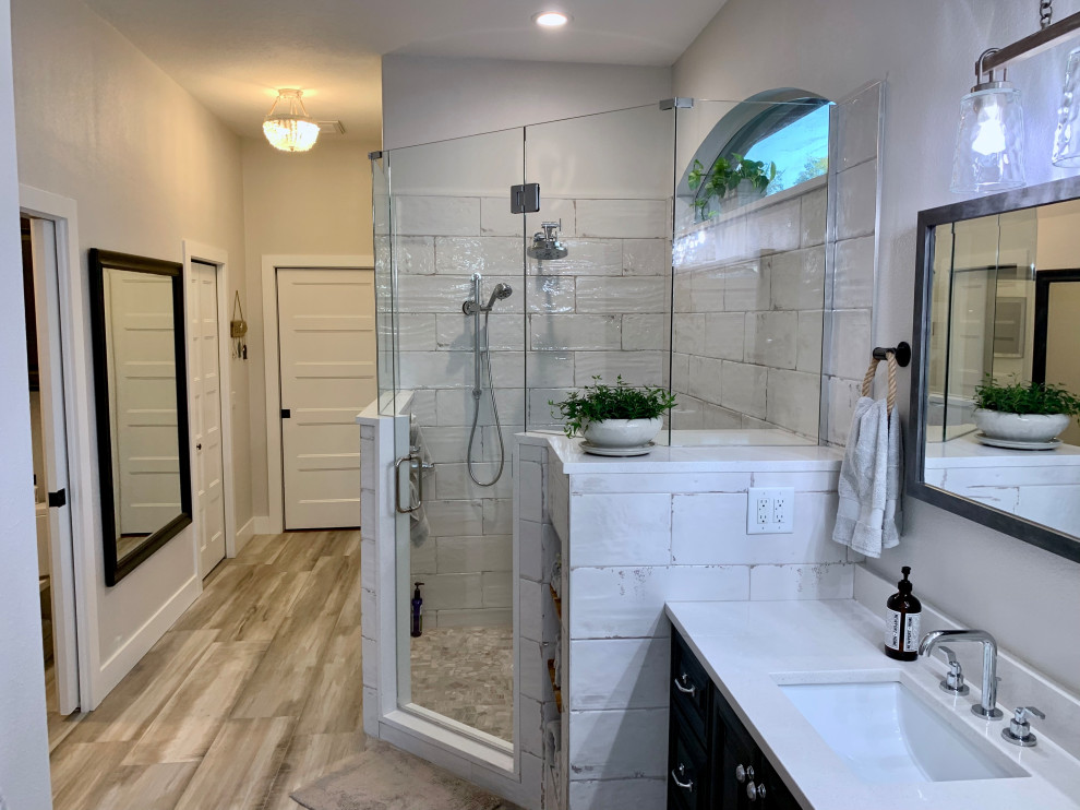 Inspiration for a contemporary ensuite bathroom in Tampa with freestanding cabinets, brown cabinets, a submerged bath, a corner shower, white tiles, ceramic tiles, grey walls, wood-effect flooring, engineered stone worktops, grey floors, white worktops, an enclosed toilet, double sinks and a built in vanity unit.