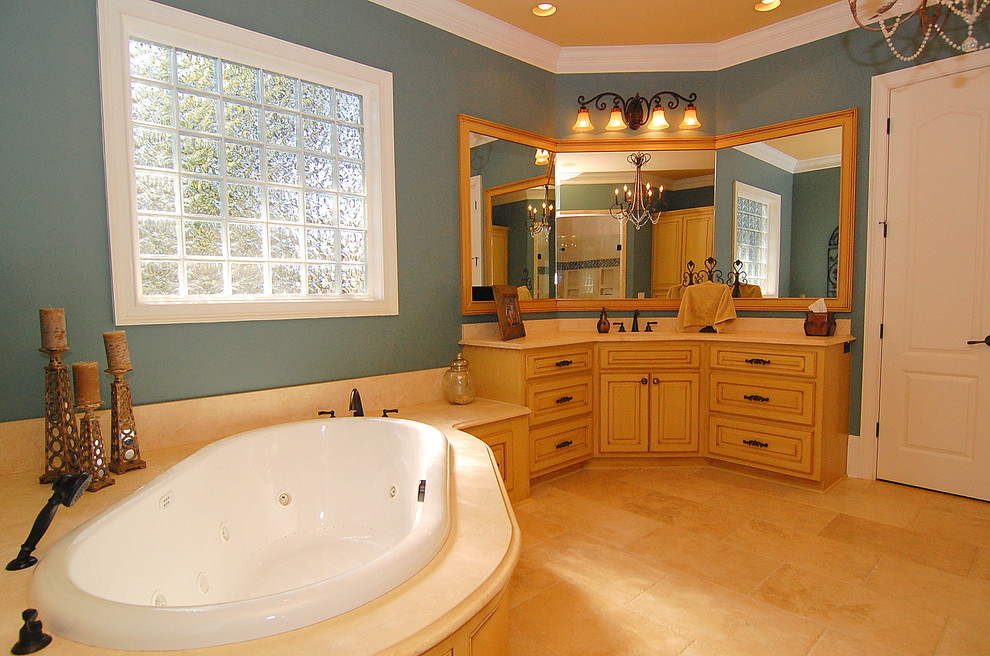 Photo of a large traditional master bathroom in Charleston with a drop-in tub, blue walls, ceramic floors, an undermount sink, beige floor, a corner shower, beige tile, granite benchtops, a hinged shower door, raised-panel cabinets and yellow cabinets.