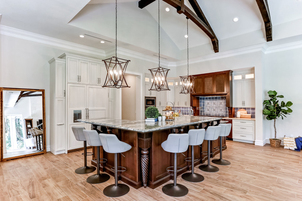 This is an example of a large transitional l-shaped open plan kitchen in Tampa with light hardwood floors, brown floor, an undermount sink, recessed-panel cabinets, beige cabinets, granite benchtops, grey splashback, ceramic splashback, panelled appliances, with island and multi-coloured benchtop.