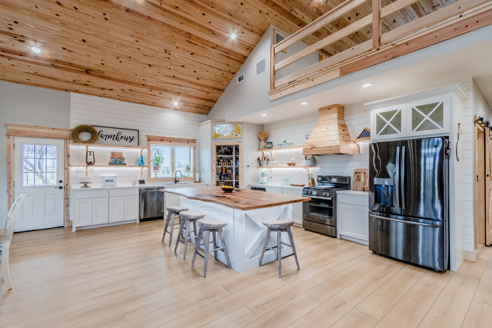 Mid-sized country l-shaped eat-in kitchen in Houston with a farmhouse sink, shaker cabinets, white cabinets, wood benchtops, white splashback, shiplap splashback, stainless steel appliances, vinyl floors, with island, beige floor, beige benchtop and wood.