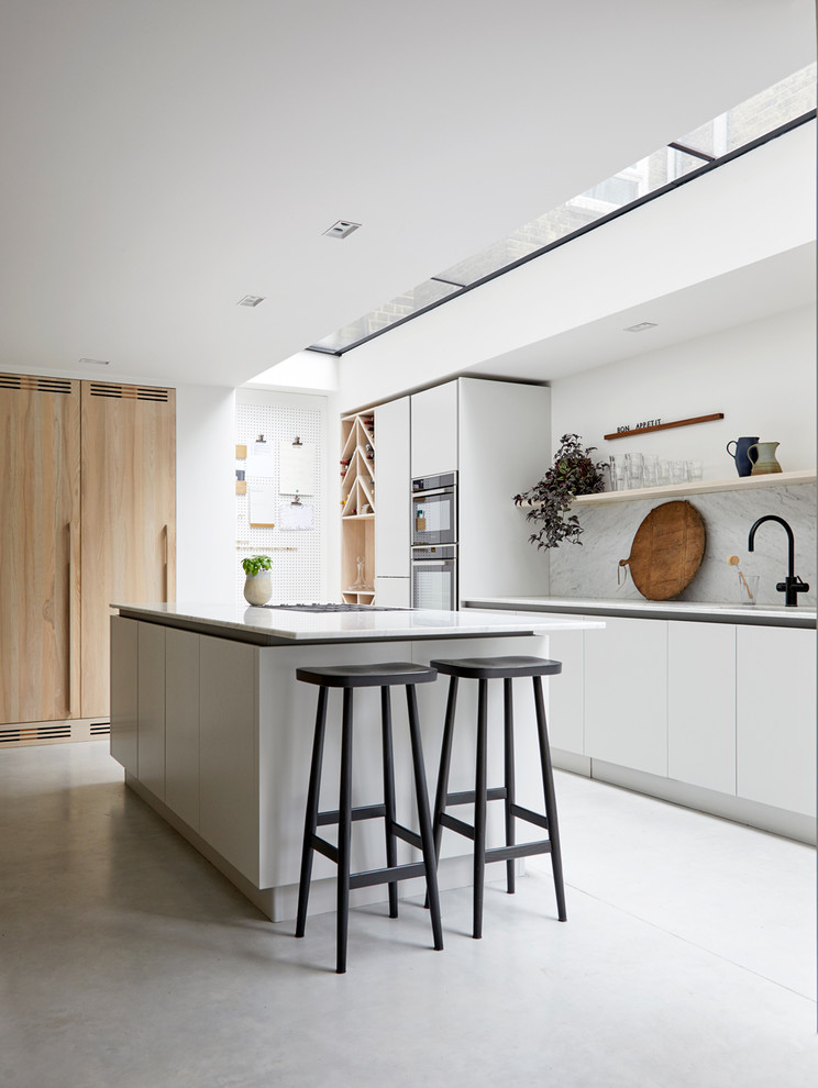 Large contemporary galley open plan kitchen in London with an integrated sink, flat-panel cabinets, grey cabinets, marble benchtops, grey splashback, marble splashback, black appliances, concrete floors, with island, grey floor and grey benchtop.