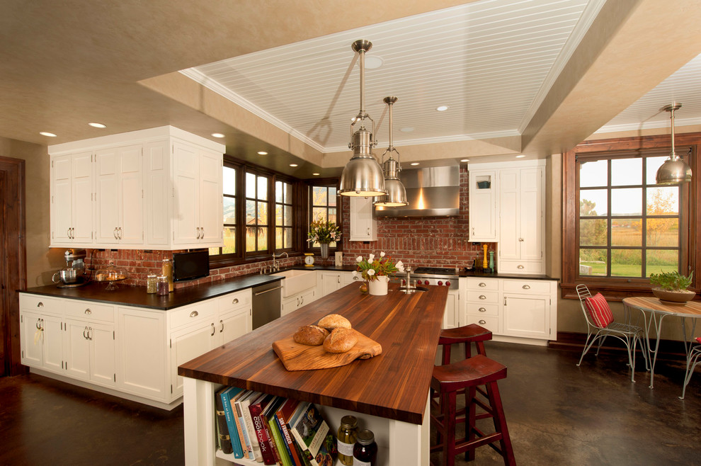 This is an example of a country eat-in kitchen in Other with a farmhouse sink, shaker cabinets, white cabinets, wood benchtops and stainless steel appliances.