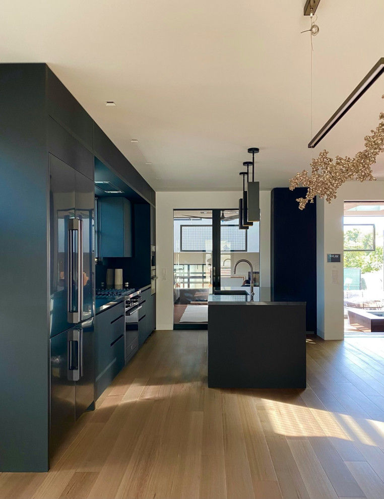 This is an example of a small modern single-wall eat-in kitchen in San Diego with a drop-in sink, flat-panel cabinets, black cabinets, marble benchtops, black splashback, marble splashback, black appliances, light hardwood floors, with island, brown floor and black benchtop.