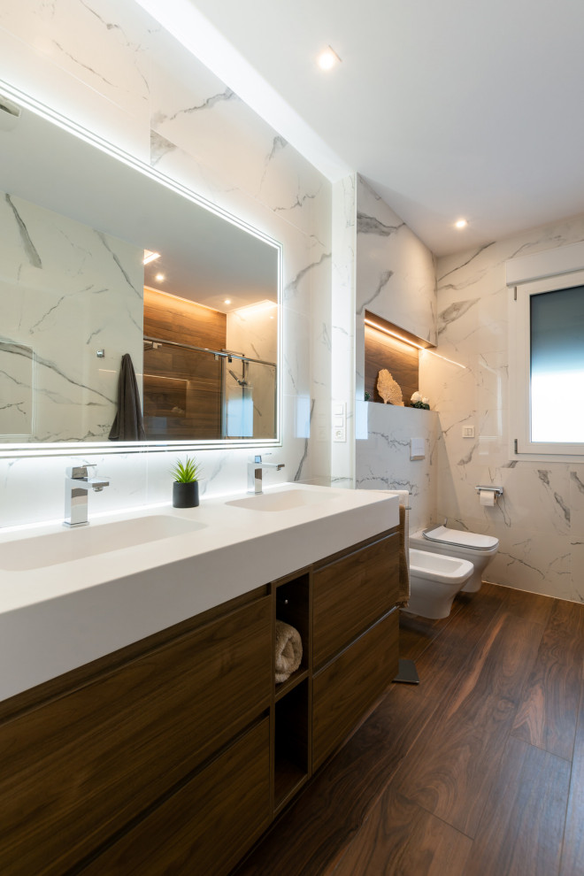 Exempel på ett mellanstort klassiskt vit vitt en-suite badrum, med släta luckor, skåp i mörkt trä, en kantlös dusch, en vägghängd toalettstol, grå kakel, keramikplattor, grå väggar, klinkergolv i keramik, ett integrerad handfat, bänkskiva i akrylsten, brunt golv och dusch med skjutdörr