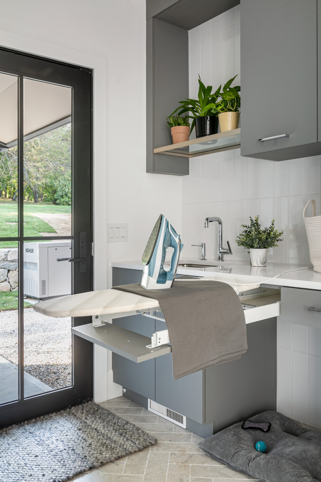 Large contemporary galley utility room in New York with an undermount sink, flat-panel cabinets, grey cabinets, quartzite benchtops, white splashback, subway tile splashback, white walls, porcelain floors, a side-by-side washer and dryer, beige floor and white benchtop.