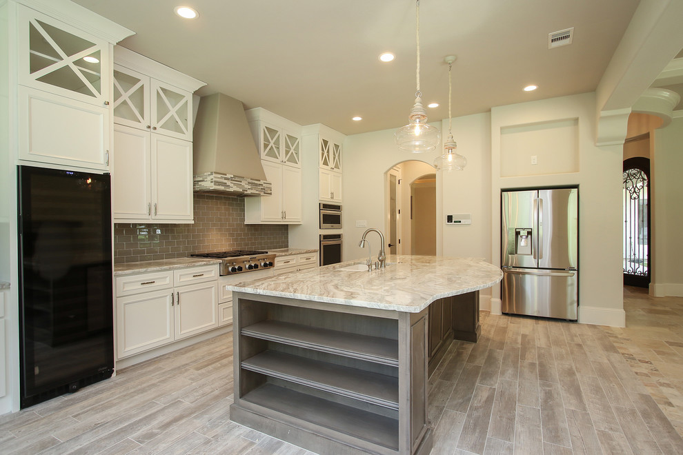 This is an example of a large mediterranean u-shaped open plan kitchen in Houston with an undermount sink, raised-panel cabinets, white cabinets, granite benchtops, ceramic splashback, stainless steel appliances, with island, beige splashback and beige floor.