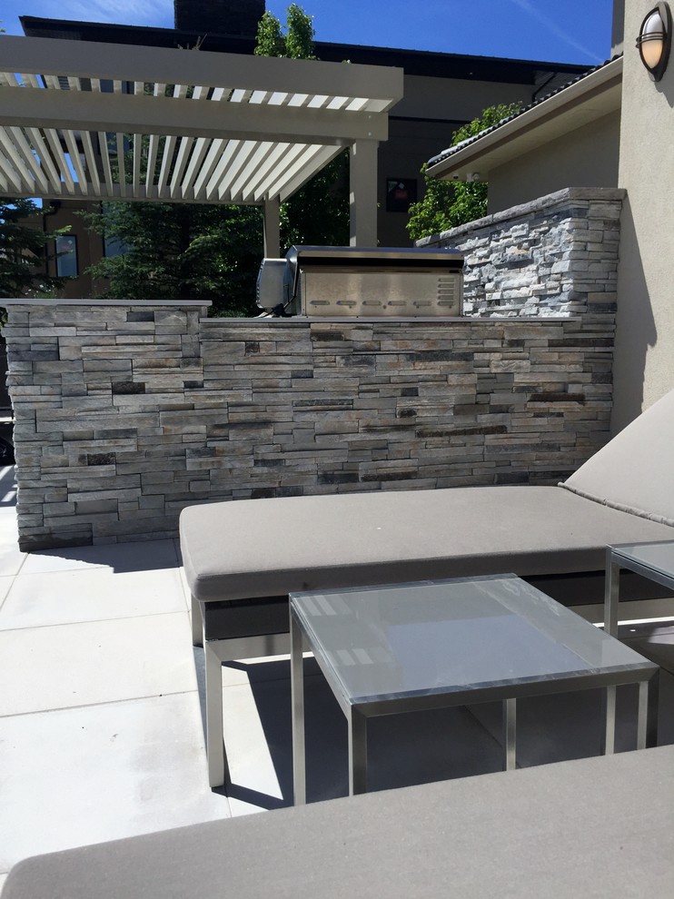 Large modern backyard patio in Boise with an outdoor kitchen, concrete pavers and a pergola.