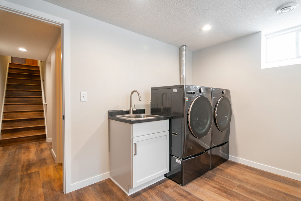 Mid-sized traditional galley utility room in Other with a single-bowl sink, shaker cabinets, white cabinets, laminate benchtops, brown walls, vinyl floors, a side-by-side washer and dryer, brown floor and black benchtop.