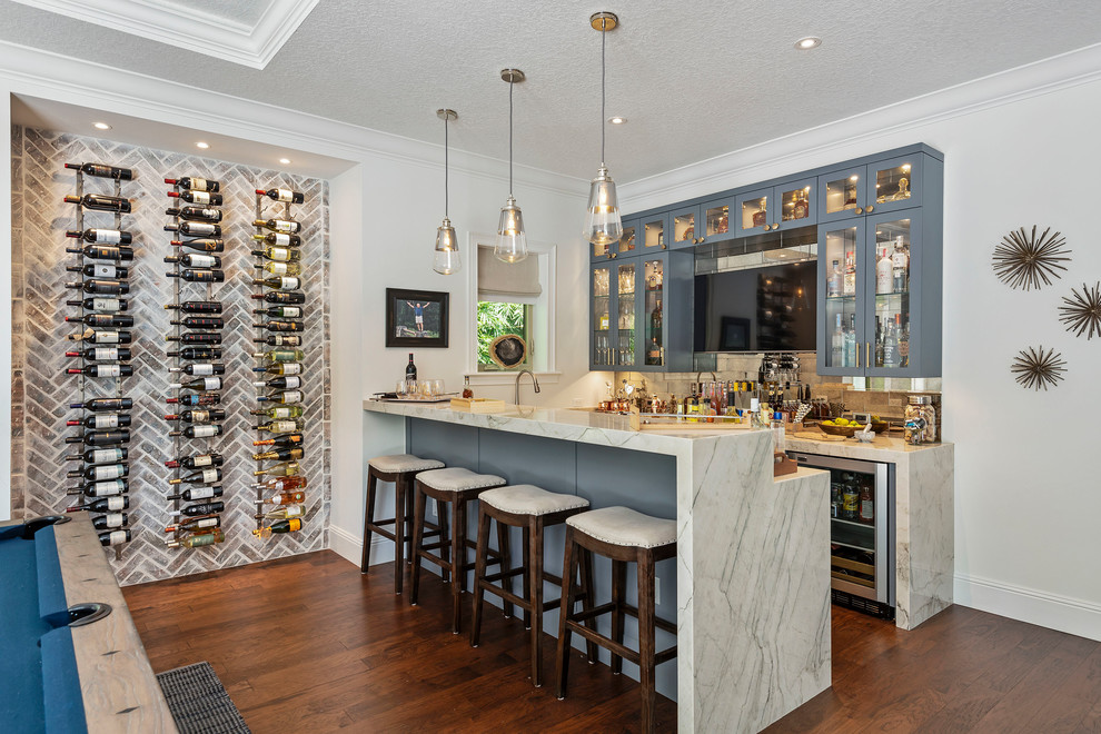 Photo of a beach style seated home bar in Orlando with glass-front cabinets, grey cabinets, marble benchtops, metal splashback, dark hardwood floors and white benchtop.