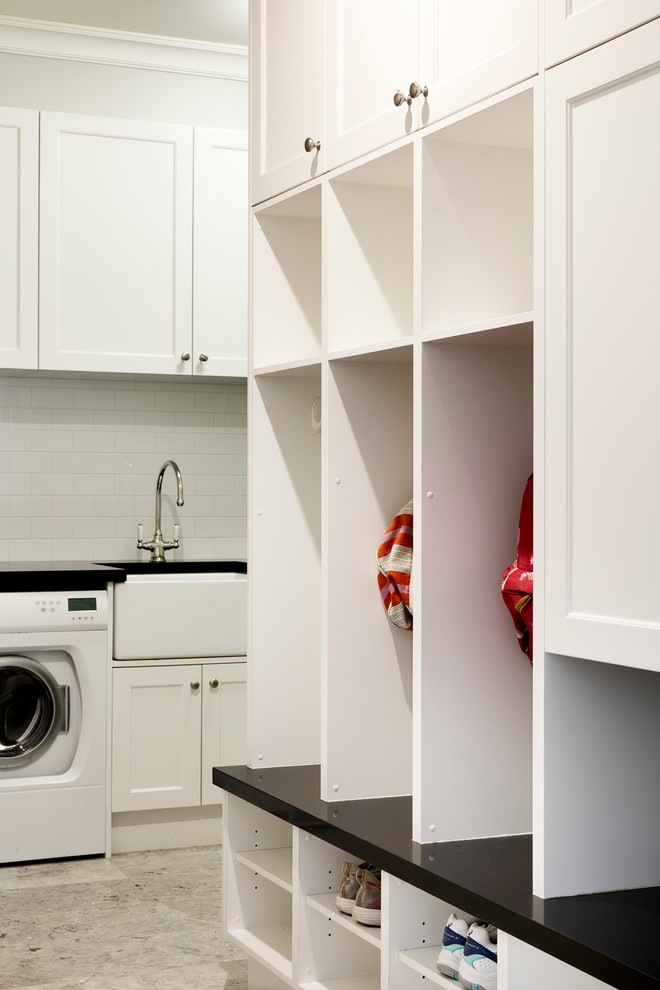 Inspiration for a transitional l-shaped dedicated laundry room in Sydney with a farmhouse sink, shaker cabinets, white cabinets, granite benchtops, grey walls, limestone floors and a side-by-side washer and dryer.