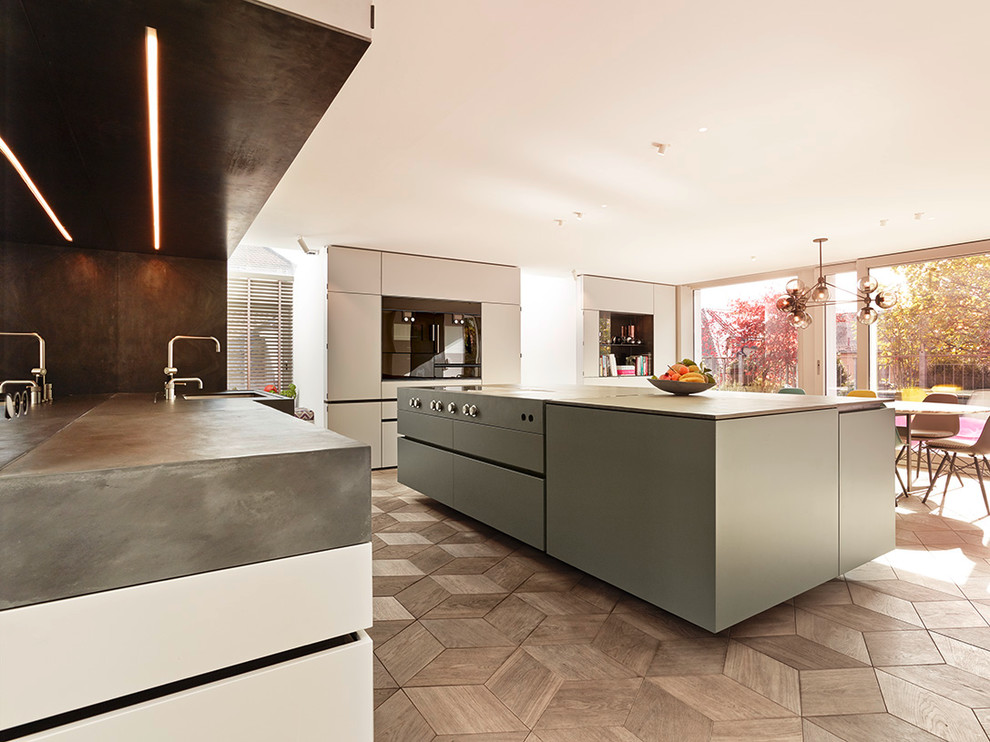 Design ideas for an expansive contemporary open plan kitchen in Munich with an undermount sink, flat-panel cabinets, grey cabinets, concrete benchtops, black appliances, medium hardwood floors and with island.