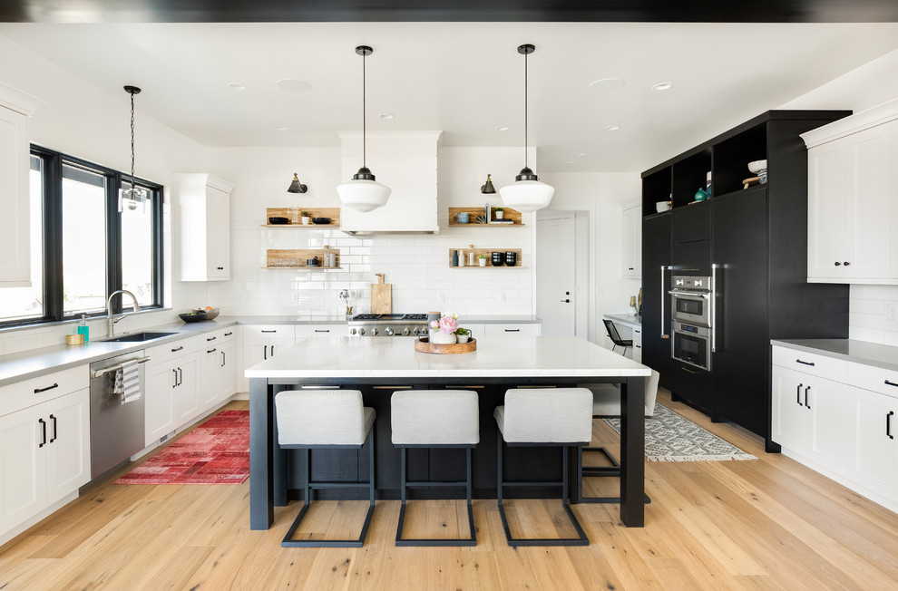 This is an example of a transitional kitchen in Salt Lake City with an undermount sink, shaker cabinets, white splashback, stainless steel appliances, light hardwood floors, with island, subway tile splashback, beige floor and grey benchtop.