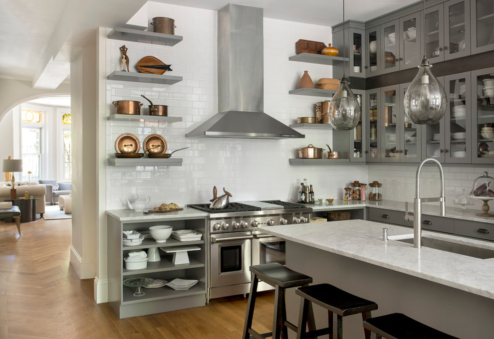 Inspiration for a large transitional l-shaped open plan kitchen in Boston with an undermount sink, glass-front cabinets, grey cabinets, marble benchtops, white splashback, porcelain splashback, stainless steel appliances, light hardwood floors and with island.