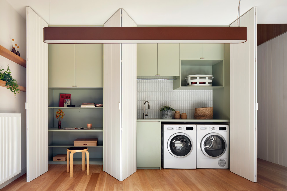 Photo of a small contemporary single-wall laundry cupboard in Melbourne with an undermount sink, flat-panel cabinets, laminate benchtops, grey splashback, ceramic splashback, green walls, a side-by-side washer and dryer, brown floor, green benchtop, green cabinets and medium hardwood floors.