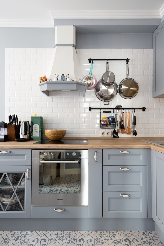 Inspiration for a traditional l-shaped kitchen in London with a drop-in sink, shaker cabinets, grey cabinets, white splashback, subway tile splashback, stainless steel appliances, grey floor and wood benchtops.