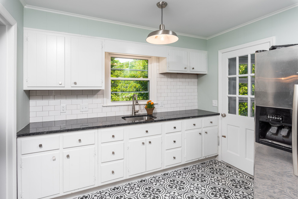 Photo of an expansive transitional u-shaped utility room in Other with an undermount sink, flat-panel cabinets, white cabinets, granite benchtops, green walls, ceramic floors, a side-by-side washer and dryer, multi-coloured floor and black benchtop.