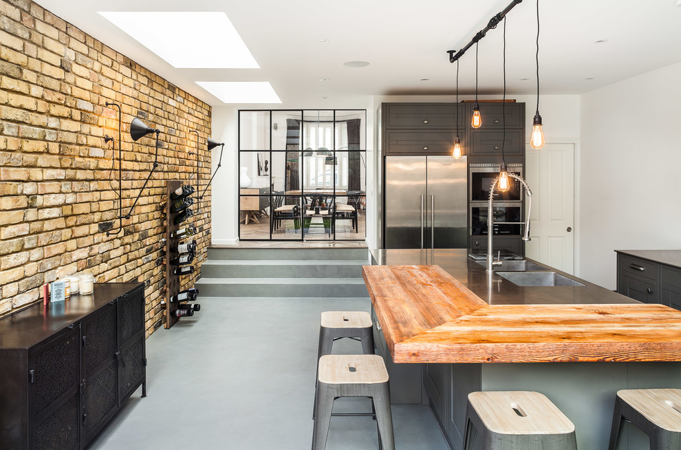 Industrial kitchen in London with a double-bowl sink, wood benchtops, stainless steel appliances, with island and grey cabinets.