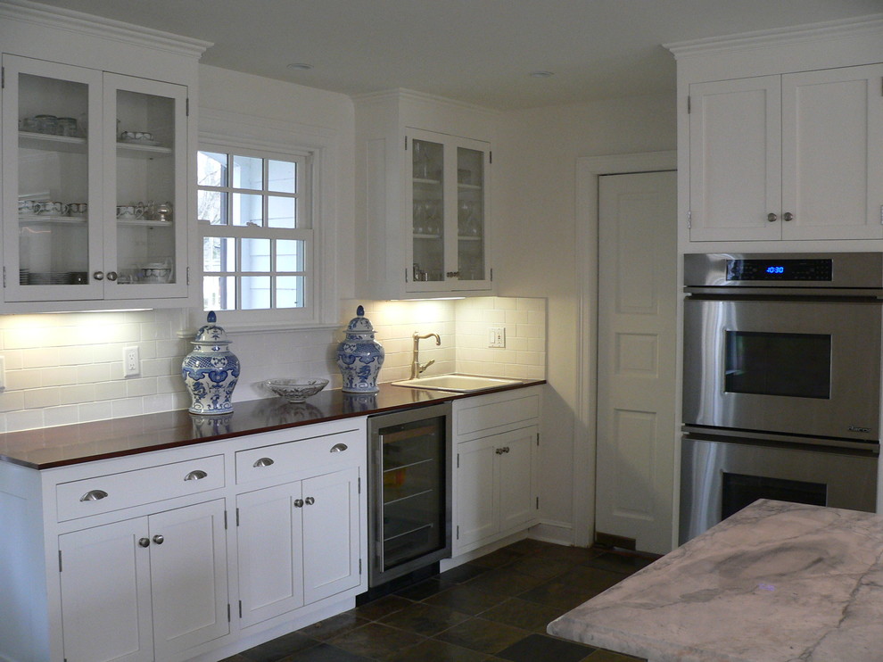 This is an example of a mid-sized traditional open plan kitchen in New York with a single-bowl sink, shaker cabinets, white cabinets, granite benchtops, white splashback, ceramic splashback, stainless steel appliances, medium hardwood floors and with island.