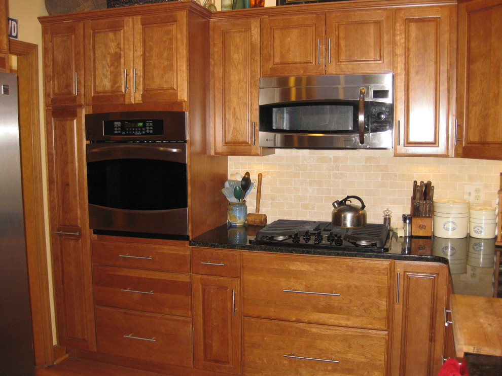 Example of a transitional u-shaped medium tone wood floor eat-in kitchen design in Boston with an undermount sink, raised-panel cabinets, medium tone wood cabinets, granite countertops, beige backsplash, subway tile backsplash, stainless steel appliances, a peninsula and black countertops