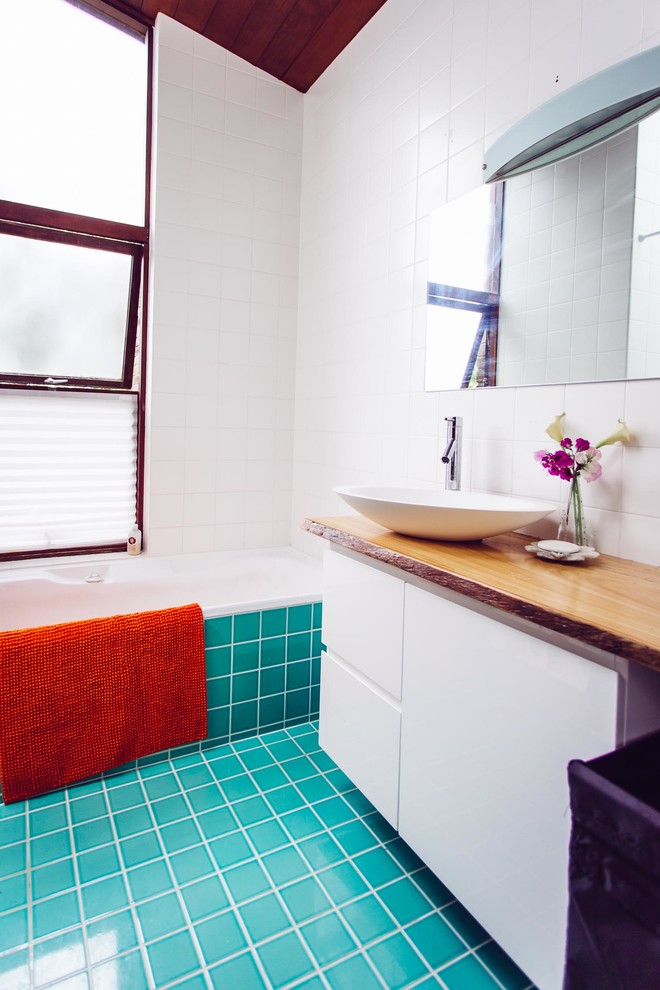 Photo of a mid-sized tropical 3/4 bathroom in Sydney with an integrated sink, beaded inset cabinets, white cabinets, solid surface benchtops, a corner tub, a corner shower, a wall-mount toilet, blue tile, glass tile, white walls and ceramic floors.