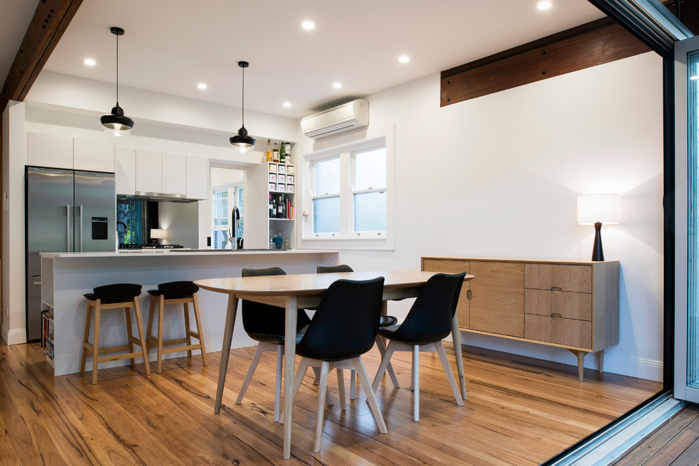 Mid-sized contemporary single-wall eat-in kitchen in Sydney with flat-panel cabinets, white cabinets, metallic splashback, mirror splashback, stainless steel appliances, medium hardwood floors, with island, brown floor and white benchtop.
