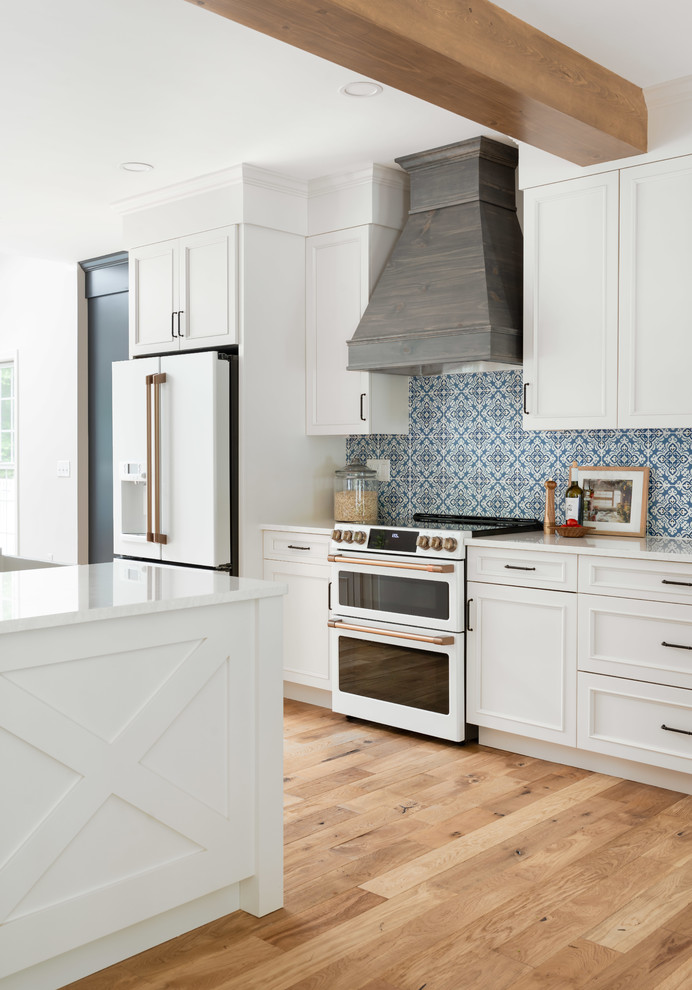 Inspiration for a large country single-wall open plan kitchen in Providence with a farmhouse sink, raised-panel cabinets, white cabinets, quartz benchtops, blue splashback, porcelain splashback, white appliances, medium hardwood floors, with island, brown floor and white benchtop.