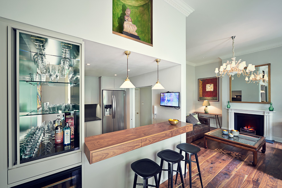 Design ideas for a transitional u-shaped seated home bar in London with wood benchtops and medium hardwood floors.