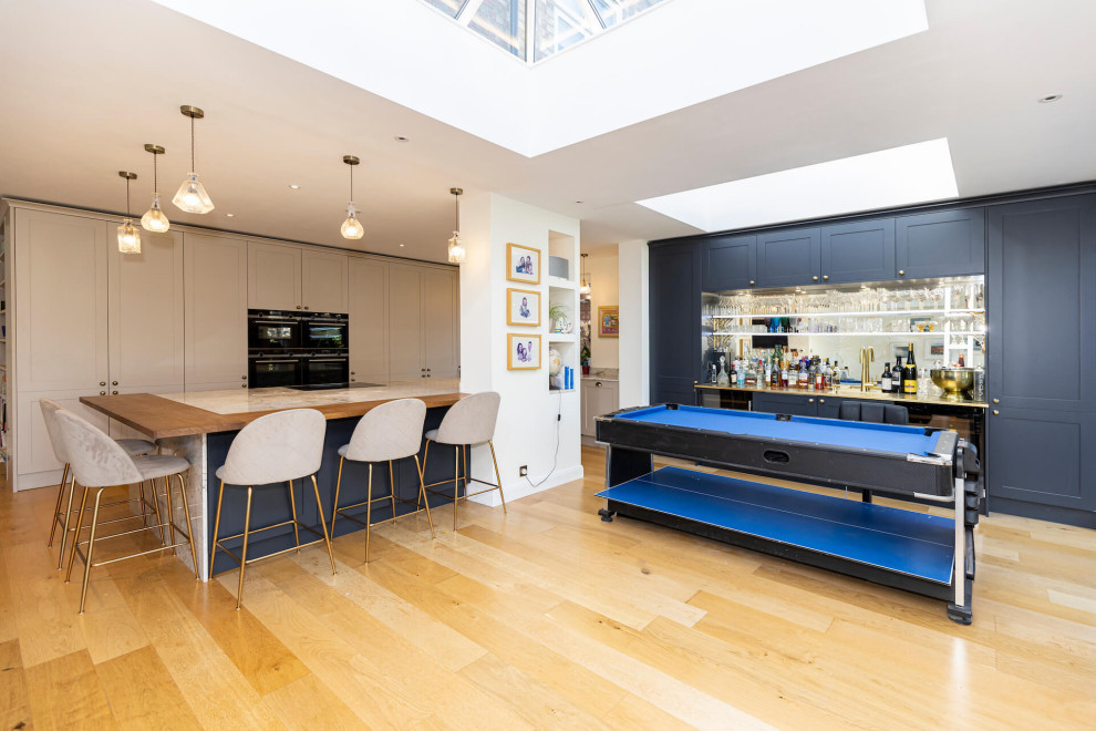 Inspiration for a large contemporary l-shaped open plan kitchen in Hertfordshire with shaker cabinets, white cabinets, granite worktops, black appliances, light hardwood flooring, an island, beige floors, blue worktops and feature lighting.