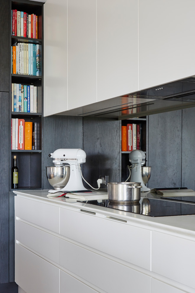 This is an example of a large l-shaped kitchen pantry in Sydney with an integrated sink, flat-panel cabinets, dark wood cabinets, marble benchtops, metallic splashback, mirror splashback, black appliances, light hardwood floors, with island and brown floor.