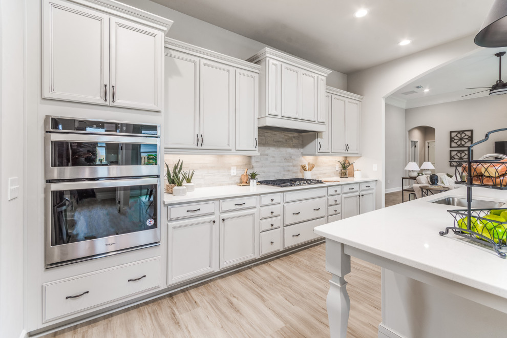 Mid-sized l-shaped eat-in kitchen in Other with a single-bowl sink, grey cabinets, quartzite benchtops, beige splashback, stone tile splashback, stainless steel appliances, vinyl floors, with island, brown floor and white benchtop.