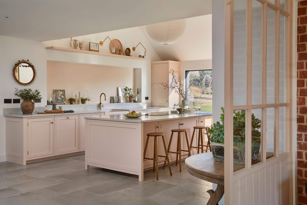 Large country grey and pink single-wall open plan kitchen in London with a belfast sink, shaker cabinets, pink cabinets, quartz worktops, pink splashback, black appliances, ceramic flooring, an island, multi-coloured floors, grey worktops and a vaulted ceiling.