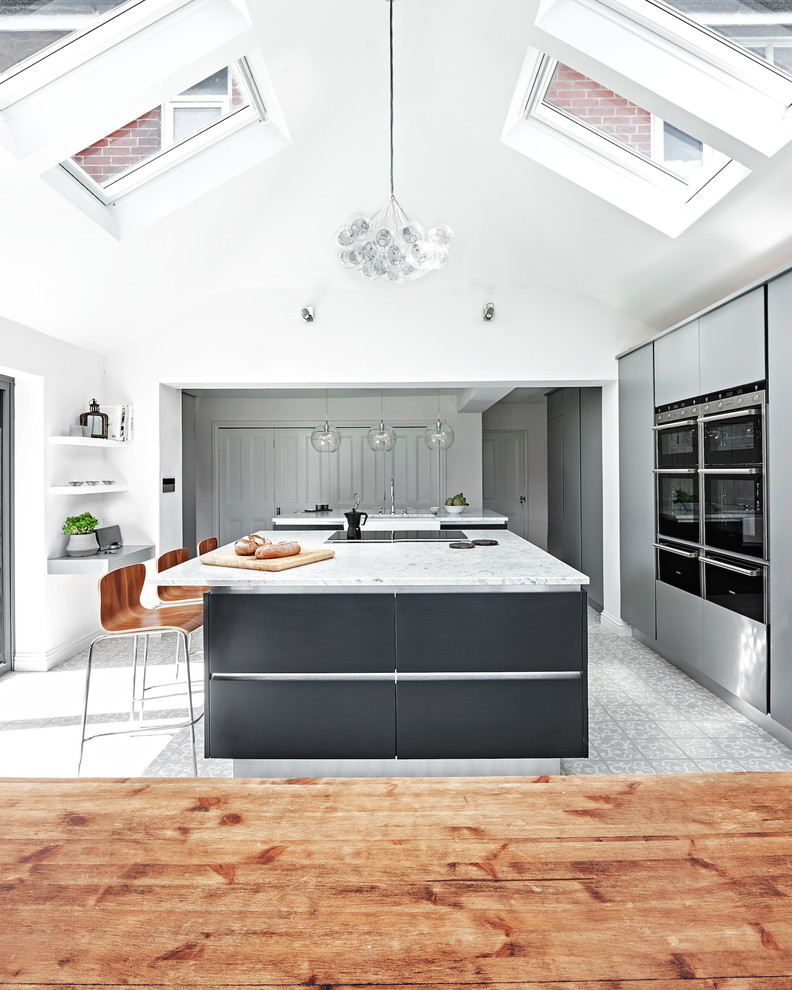 This is an example of a large contemporary single-wall eat-in kitchen in Wiltshire with a farmhouse sink, flat-panel cabinets, grey cabinets, marble benchtops, stainless steel appliances, ceramic floors and multiple islands.