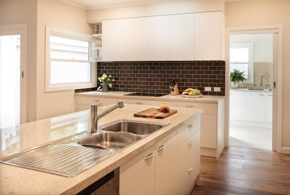 Inspiration for a mid-sized transitional l-shaped eat-in kitchen in Melbourne with a double-bowl sink, flat-panel cabinets, beige cabinets, quartz benchtops, brown splashback, subway tile splashback, stainless steel appliances, medium hardwood floors and with island.