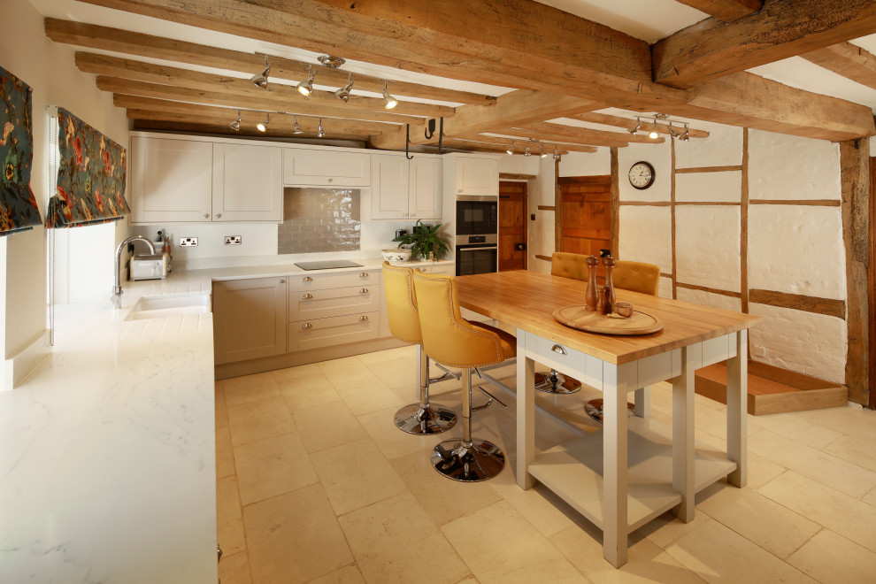 Photo of a country l-shaped kitchen in Kent with a farmhouse sink, shaker cabinets, grey cabinets, stainless steel appliances, with island, beige floor, white benchtop and exposed beam.