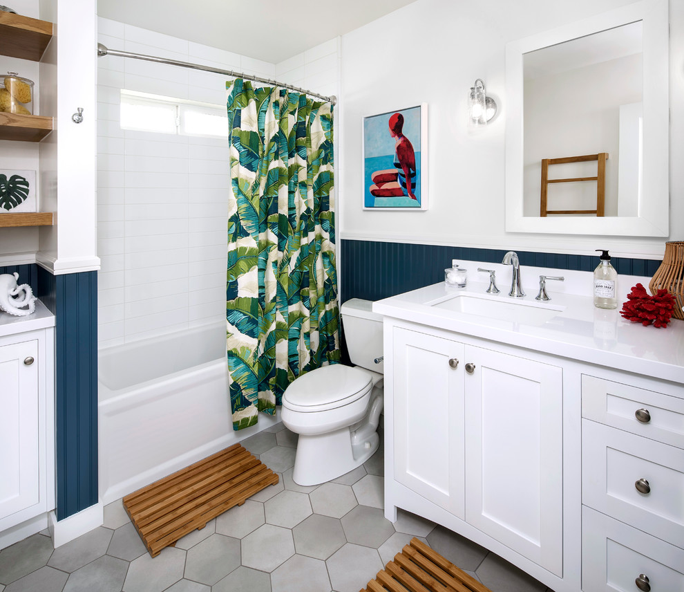 Photo of a mid-sized beach style bathroom in San Francisco with shaker cabinets, white cabinets, an alcove tub, a shower/bathtub combo, a two-piece toilet, white tile, blue walls, ceramic floors, a drop-in sink, engineered quartz benchtops and grey floor.