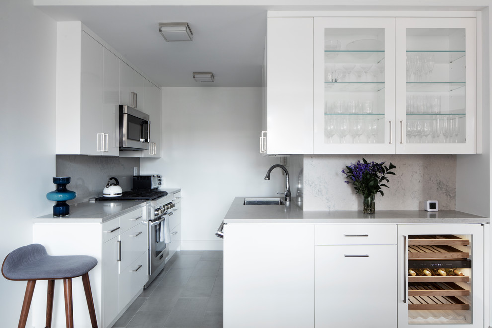 Photo of a mid-sized contemporary l-shaped kitchen in New York with an undermount sink, glass-front cabinets, white cabinets, solid surface benchtops, grey splashback, stone slab splashback, stainless steel appliances, porcelain floors, no island, grey floor and grey benchtop.