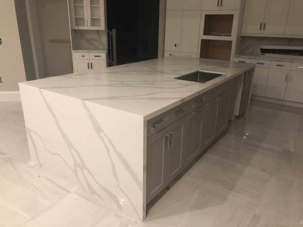 This is an example of a large contemporary l-shaped eat-in kitchen in Miami with a triple-bowl sink, flat-panel cabinets, grey cabinets, quartz benchtops, white splashback, stone slab splashback, stainless steel appliances, porcelain floors, with island, grey floor and white benchtop.