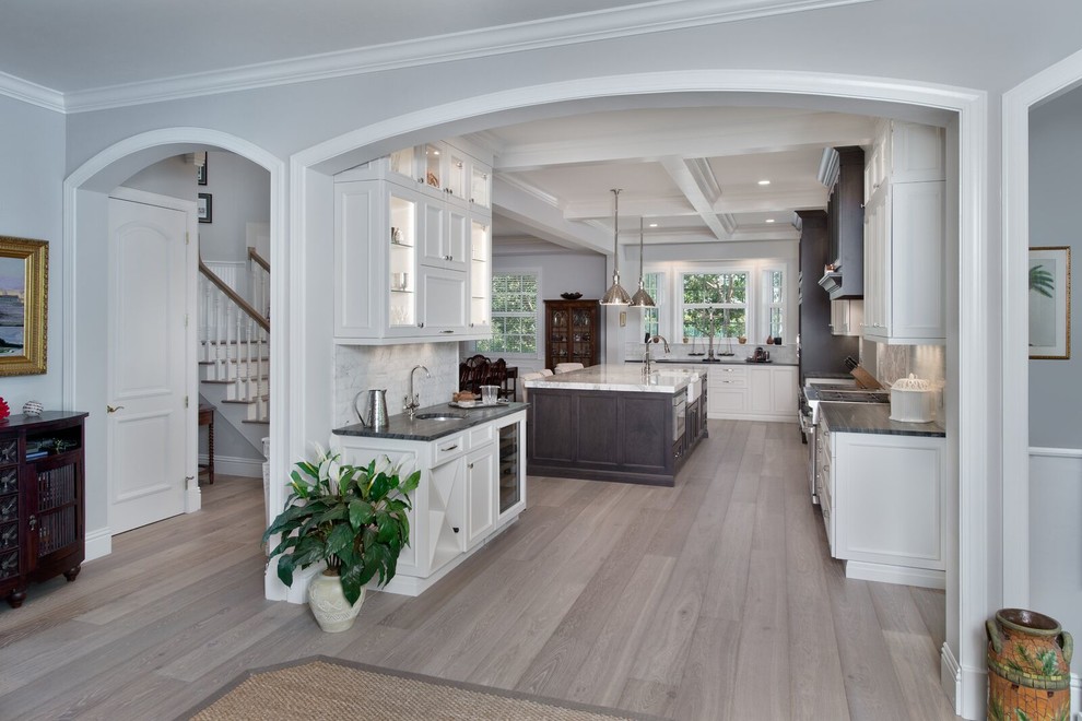 Large transitional kitchen in Miami with glass-front cabinets, white cabinets, white splashback, marble splashback, panelled appliances, light hardwood floors, with island, brown floor, a farmhouse sink and marble benchtops.