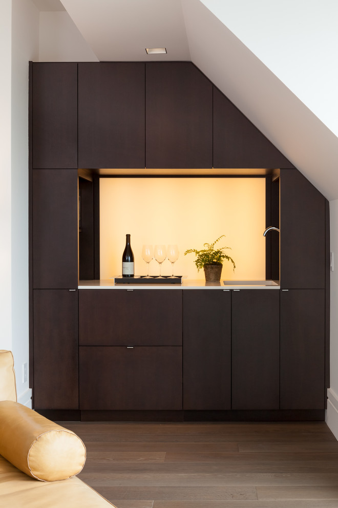 Small modern single-wall wet bar in San Francisco with an undermount sink, flat-panel cabinets, brown cabinets, quartz benchtops, white splashback, glass sheet splashback, light hardwood floors, brown floor and white benchtop.