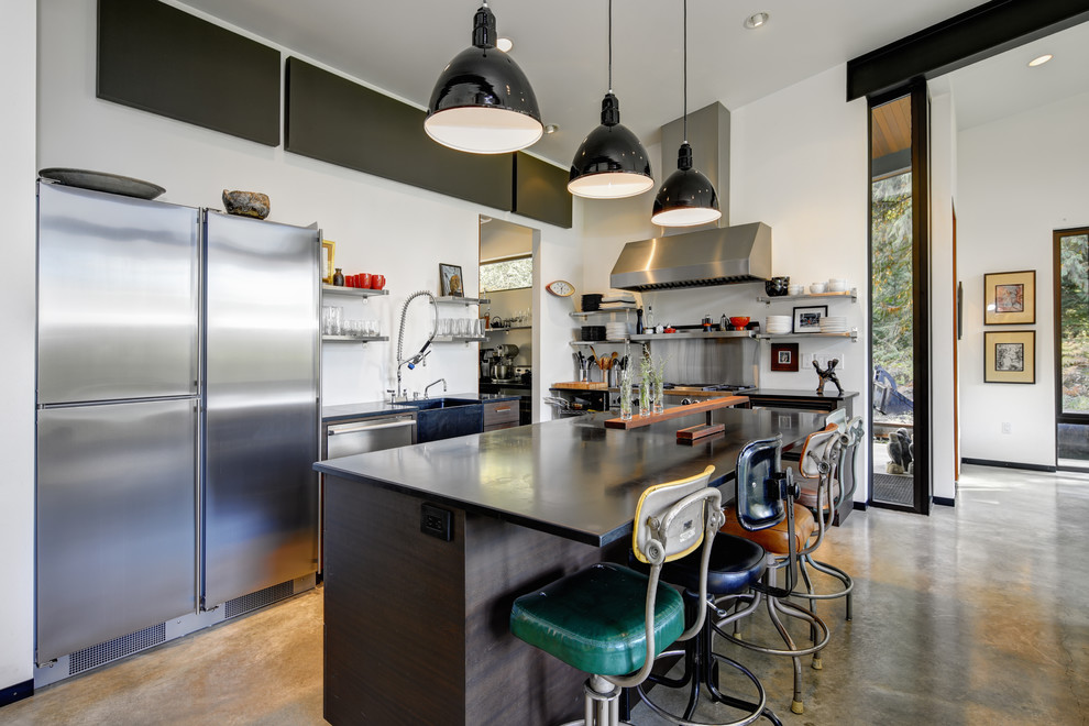 This is an example of an industrial l-shaped kitchen in Seattle with a farmhouse sink, flat-panel cabinets, dark wood cabinets, stainless steel appliances, concrete floors, with island and grey floor.