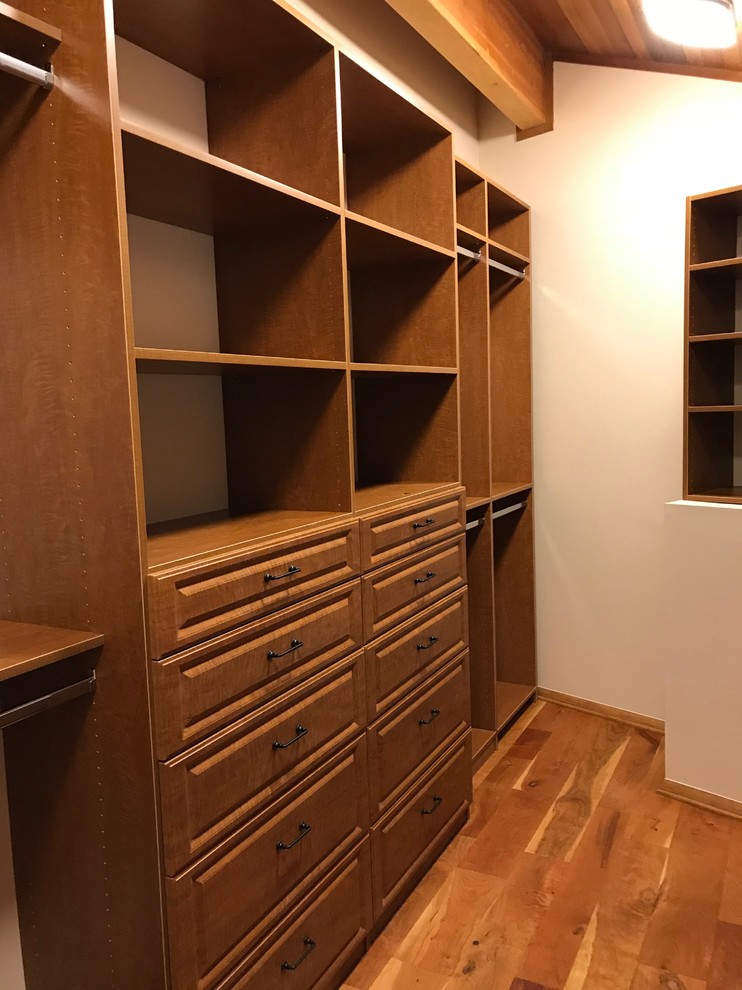 This is an example of a mid-sized traditional gender-neutral walk-in wardrobe in Other with raised-panel cabinets, medium wood cabinets, medium hardwood floors and brown floor.