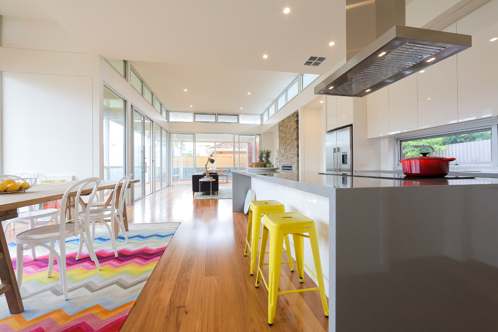 Photo of a mid-sized contemporary galley eat-in kitchen in Adelaide with a double-bowl sink, white cabinets, quartz benchtops, glass sheet splashback, stainless steel appliances, medium hardwood floors and with island.