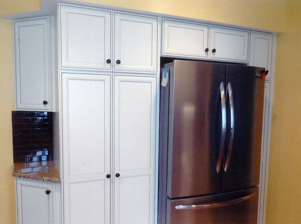 Example of a mid-sized transitional l-shaped laminate floor and yellow floor kitchen pantry design with an undermount sink, recessed-panel cabinets, white cabinets, granite countertops, brown backsplash, ceramic backsplash, stainless steel appliances, no island and beige countertops