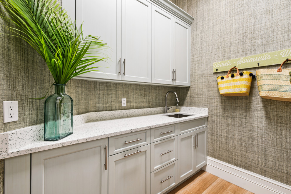 Large tropical u-shaped laundry room in Other with an undermount sink, beaded inset cabinets, white cabinets, quartzite benchtops, blue splashback, glass tile splashback, light hardwood floors, brown floor, beige benchtop and wood.